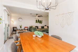 Un comedor con una mesa de madera, sillas, un ventilador de techo y un sofá verde al fondo.