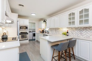 Uma cozinha moderna com armários brancos, uma ilha central com banquetas, eletrodomésticos embutidos e um backsplash de azulejos em padrão herringbone.