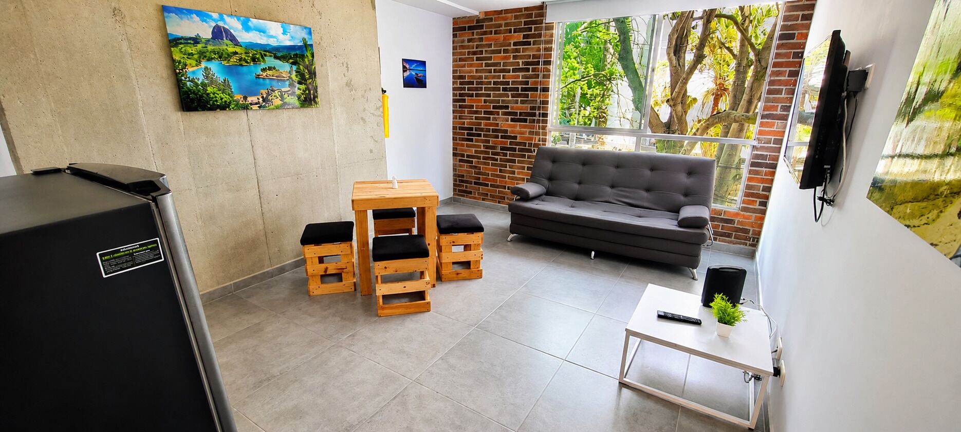 Un salon avec un canapé, une table basse et un téléviseur. On y trouve des tabourets en bois et un tableau accroché au mur.