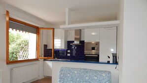 Cozinha compacta com forno embutido, janela com vista para vegetação e cadeira estampada.
