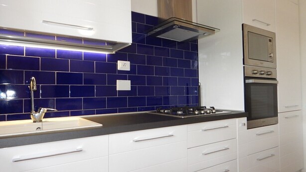 Uma cozinha moderna com armários brancos, um revestimento de azulejos azuis, um exaustor de aço inoxidável e um forno embutido.