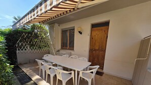 Um pátio com mesa e cadeiras brancas, uma porta de madeira e uma parede branca.