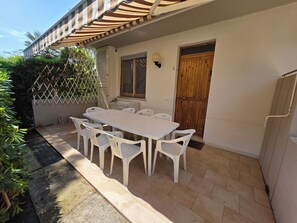 Eine Terrasse mit einem weißen Tisch und Stühlen, einer Holztür und einer weißen Wand.