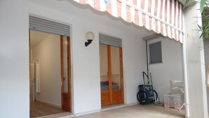 Um edifício com um pátio ladrilhado, portas de madeira, um candeeiro fixado na parede e um suporte para bicicletas.