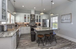 A modern kitchen with white cabinets, a stainless steel refrigerator, and a large island with bar stools. - Rising Sun Pool Elevator  Pet Beach Access (Eastpoint)