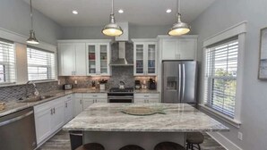 A kitchen with white cabinets, a central island with stools, stainless steel appliances, and pendant lighting. - Rising Sun Pool Elevator  Pet Beach Access (Eastpoint)
