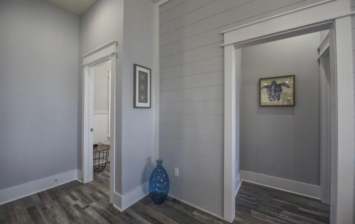 A hallway with a wooden floor, a blue vase, and two framed pictures on the walls.