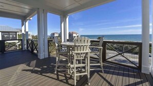 A covered outdoor deck with Adirondack chairs and a table, overlooking a beach and ocean. - Rising Sun Pool Elevator  Pet Beach Access (Eastpoint)