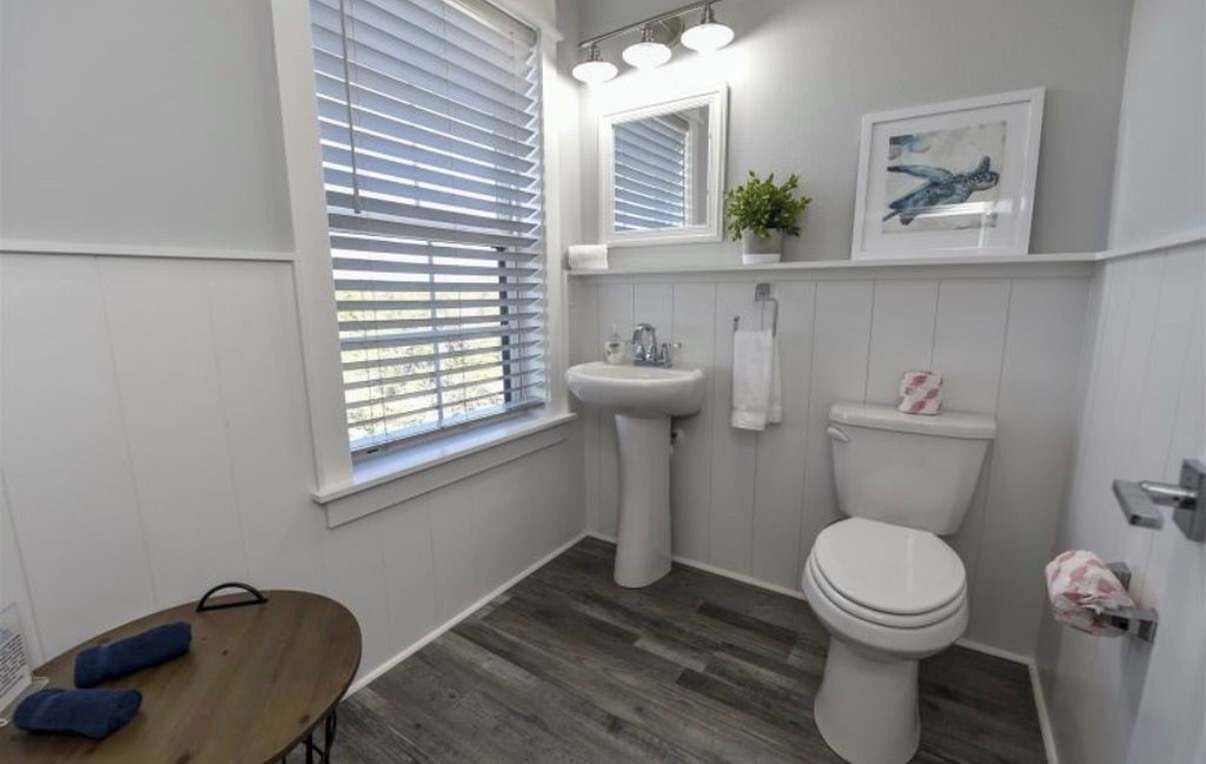 Un baño con lavamanos pedestal, inodoro y ventana con persianas.