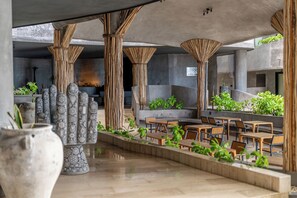 An outdoor seating area with tables and chairs, surrounded by plants and decorative columns. - Oceanfront luxury 3BR in Tankah w/ Private Beach (Tulum)