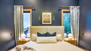 Quarto com cama grande, duas mesas de cabeceira, cabeceira e cortinas.