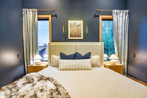 Ein Schlafzimmer mit einem großen Bett, zwei Nachttischen, einer Kopfteil und Vorhängen.