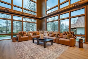 Ein geräumiges Wohnzimmer mit einer großen Eckcouch, einem Couchtisch und Blick ins Freie durch große Fenster.
