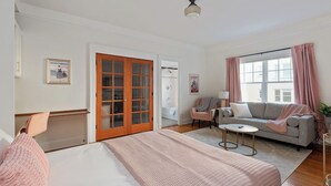 Ett sovrum med en säng, en soffa, ett litet bord, en stol, ett fönster med gardiner och en dörr som leder till ett badrum.