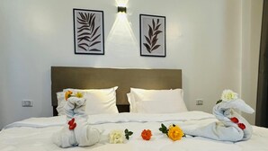 A neatly made bed with towels shaped like swans, a white wall with two framed leaf designs, and a wall-mounted light fixture. - Malak house swimming pool&garden 1 (Luxor)
