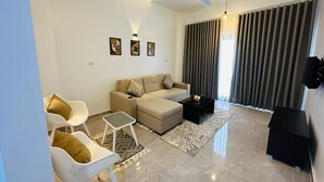 A modern living room with a sofa, chairs, a coffee table, a ceiling fan, and a large window with curtains. - Malak house swimming pool&garden 1 (Luxor)