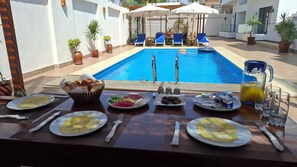 Desayuno junto a la piscina, con sillones de descanso y plantas en macetas.