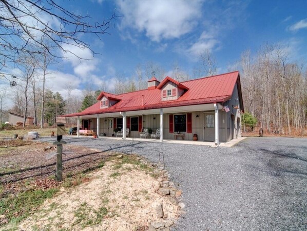A two-story house with a red roof, a covered porch, and a gravel driveway.