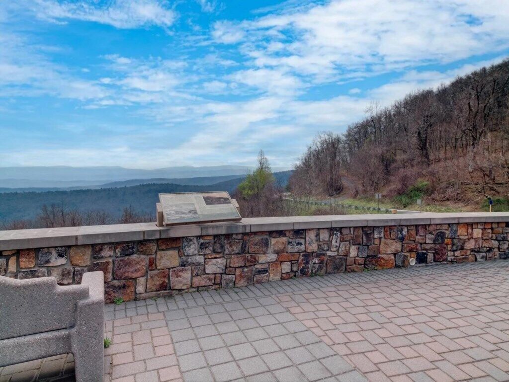 Un mur de pierre avec un banc, offrant une vue sur un paysage vallonné.