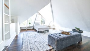 Un dormitorio abuhardillado con techos altos, una cama, un banco acolchado, una alfombra y una planta en maceta.