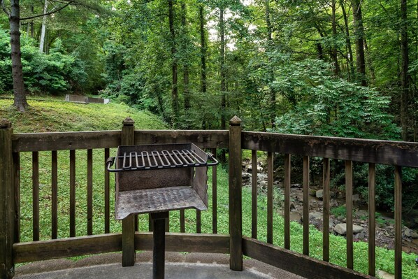 A wooden fence with a metal grill table in a forested area. - Cozy w/King Bed and Game Room! 5 Min to Parkway (Gatlinburg)