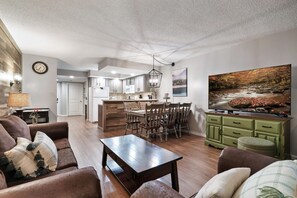 A modern living room with a wooden coffee table, brown sofas, and a dining area with wooden chairs. - Cozy w/King Bed and Game Room! 5 Min to Parkway (Gatlinburg)
