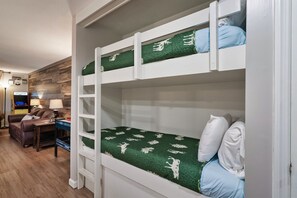 A bunk bed with green patterned bedding, a desk with a lamp, and a couch in a room with wooden flooring and a wall-mounted shelf. - Cozy w/King Bed and Game Room! 5 Min to Parkway (Gatlinburg)