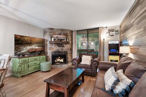 A living room with a stone fireplace, a television, a couch, and a coffee table. - Cozy w/King Bed and Game Room! 5 Min to Parkway (Gatlinburg)