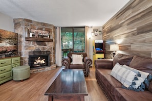 A cozy living room with a stone fireplace, a comfortable leather sofa, a wooden coffee table, and a television on a stone wall. - Cozy w/King Bed and Game Room! 5 Min to Parkway (Gatlinburg)