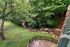 A view of a lush green forested area with a small stream, a wooden deck, and a stone wall. - Cozy w/King Bed and Game Room! 5 Min to Parkway (Gatlinburg)