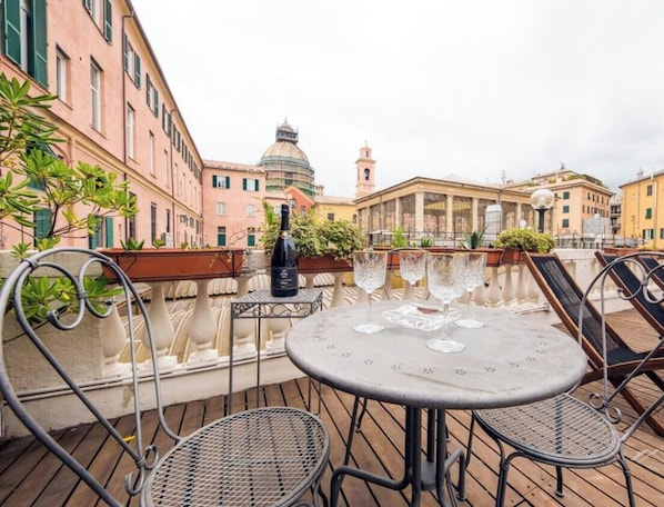 Eine Außenpatio mit einem runden Tisch und Metallstühlen, mit Blick auf eine historische Stadtlandschaft mit Kuppelbauten und einem Turm.