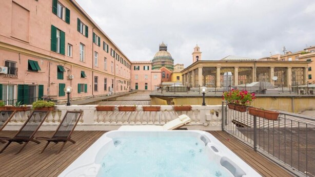 Une terrasse sur le toit dotée d’un jacuzzi, de chaises longues et offrant une vue sur des bâtiments historiques.