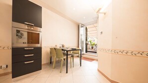 Une cuisine compacte dotée d’un four encastré, d’une table à manger avec des chaises, et offrant une vue sur un espace extérieur grâce à une porte ouverte.