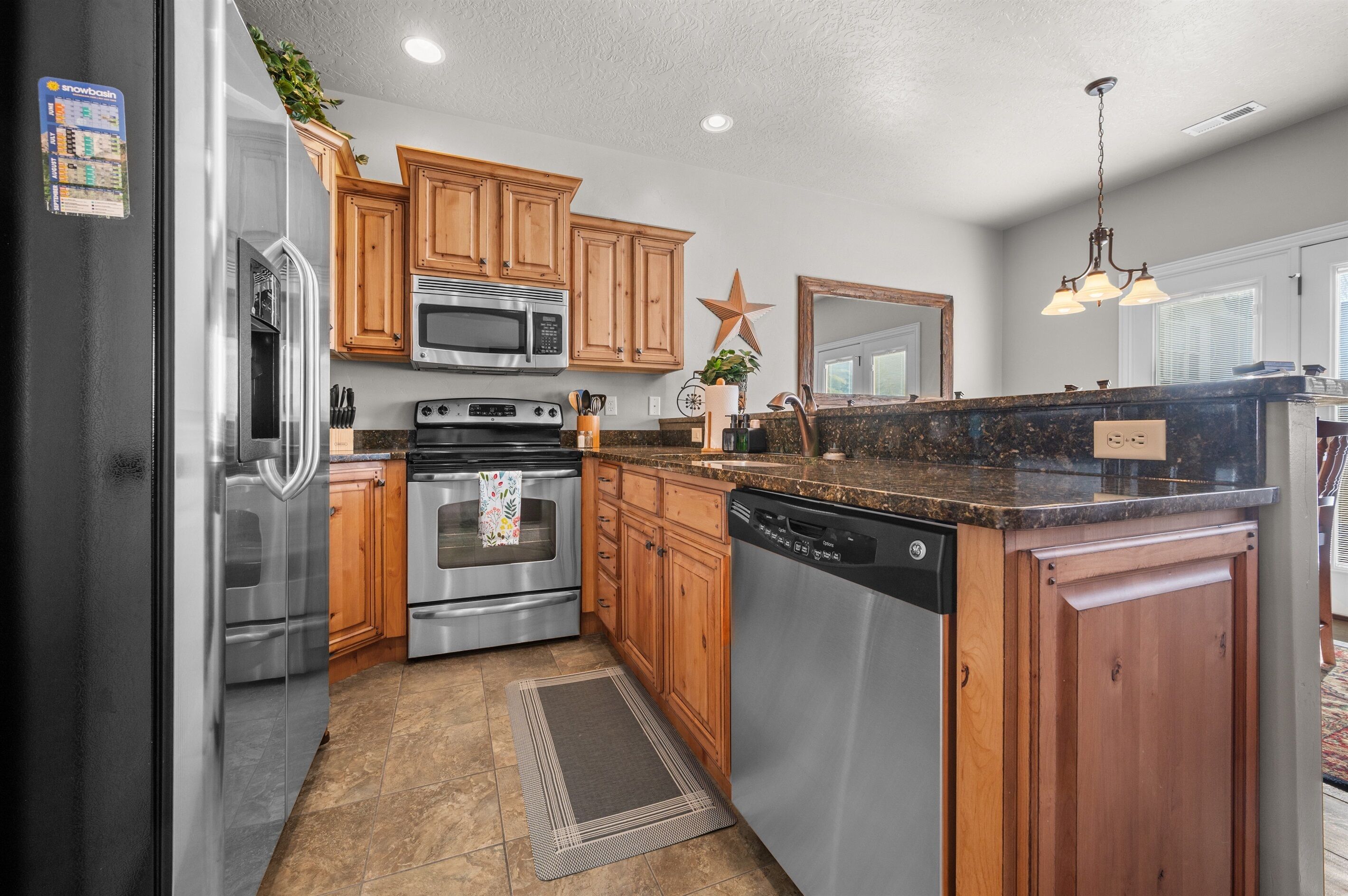 A kitchen with wooden cabinets, stainless steel appliances, a granite countertop, and a star decoration on the wall.