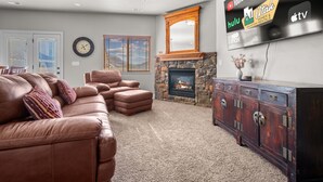 A living room with a leather couch, a stone fireplace, a flat-screen TV, and a wooden cabinet. - Aspen Tree Chalet |Snowbasin|By Pineview Reservoir (Mountain Green)