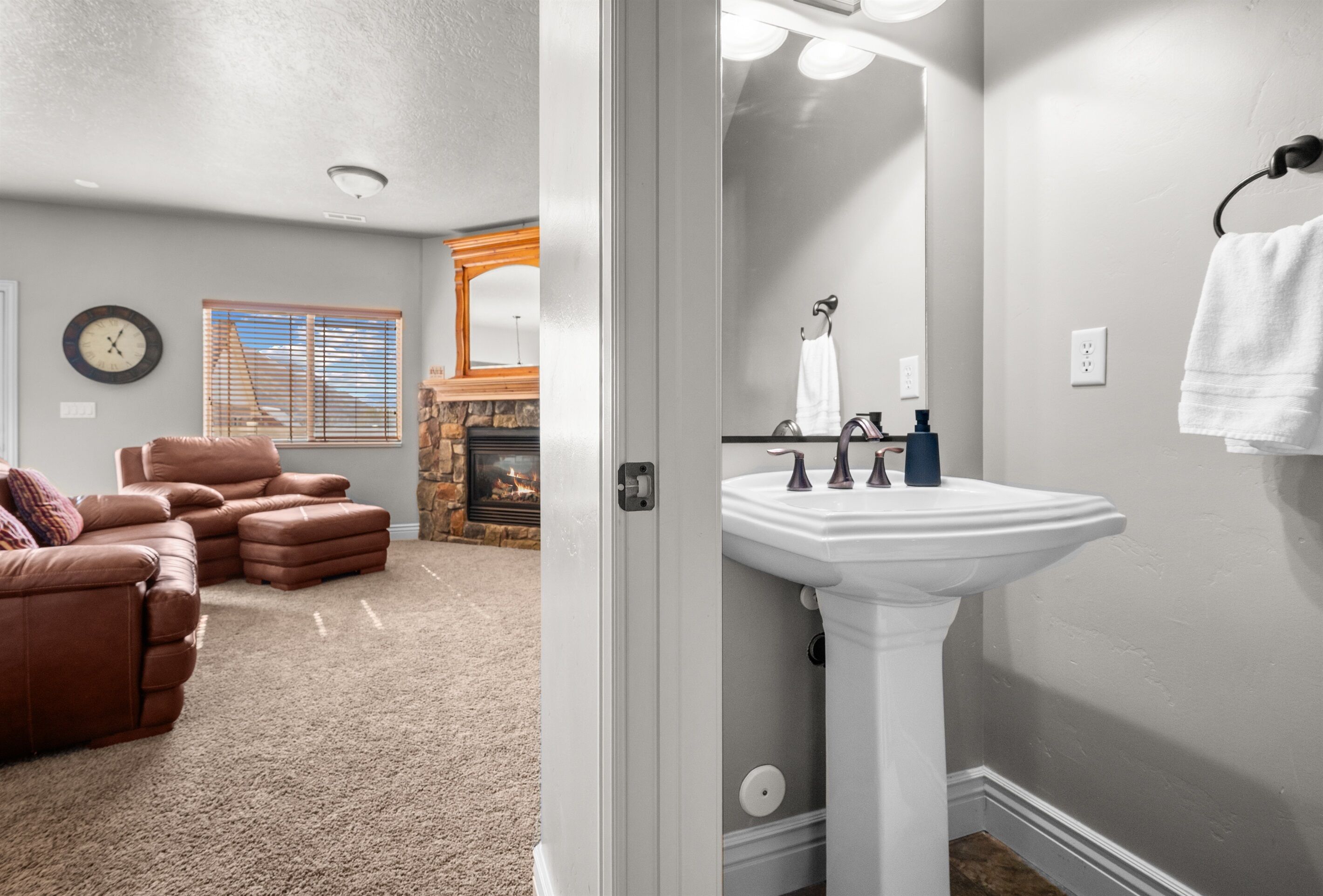 A living room with a brown leather sofa, a fireplace, and a white sink in the adjacent bathroom.