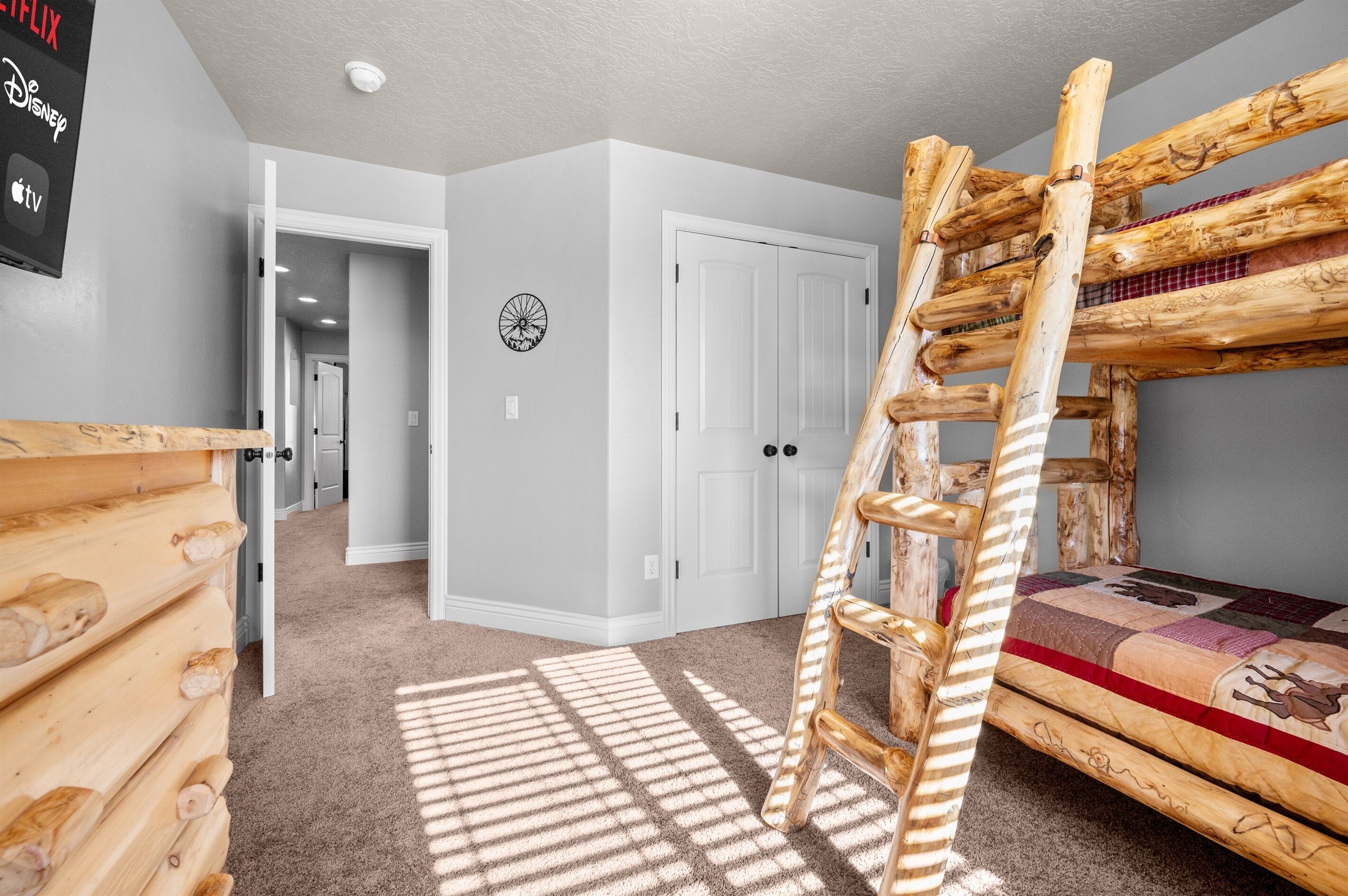A room with a bunk bed, a wooden ladder, a door, and a wall-mounted clock.