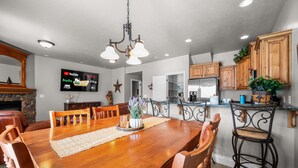 A dining area with a wooden table, chairs, and a TV displaying streaming services. - Aspen Tree Chalet |Snowbasin|By Pineview Reservoir (Mountain Green)