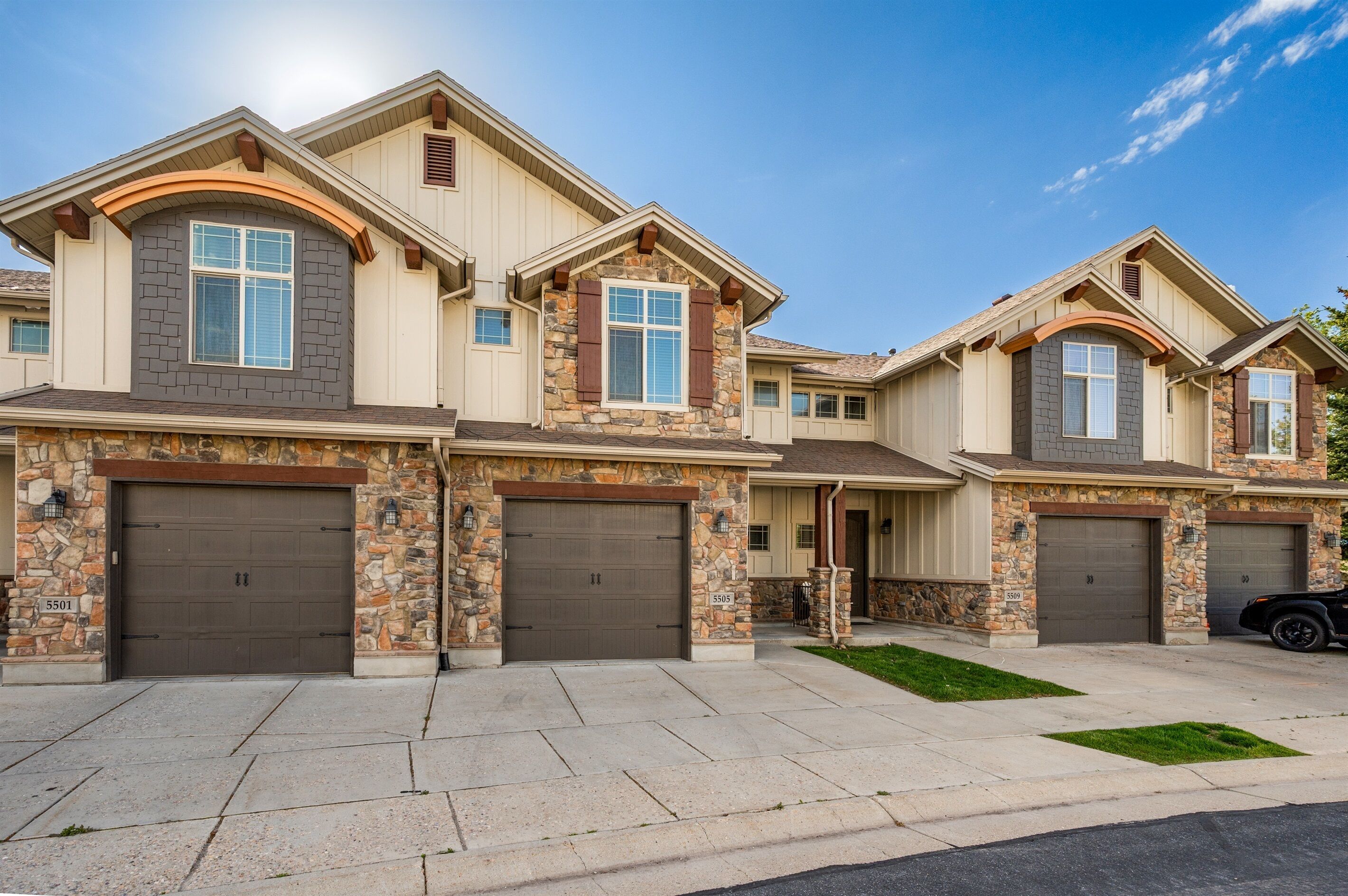 A multi-story residential building with stone and stucco exterior, multiple garage doors, and a well-maintained driveway.