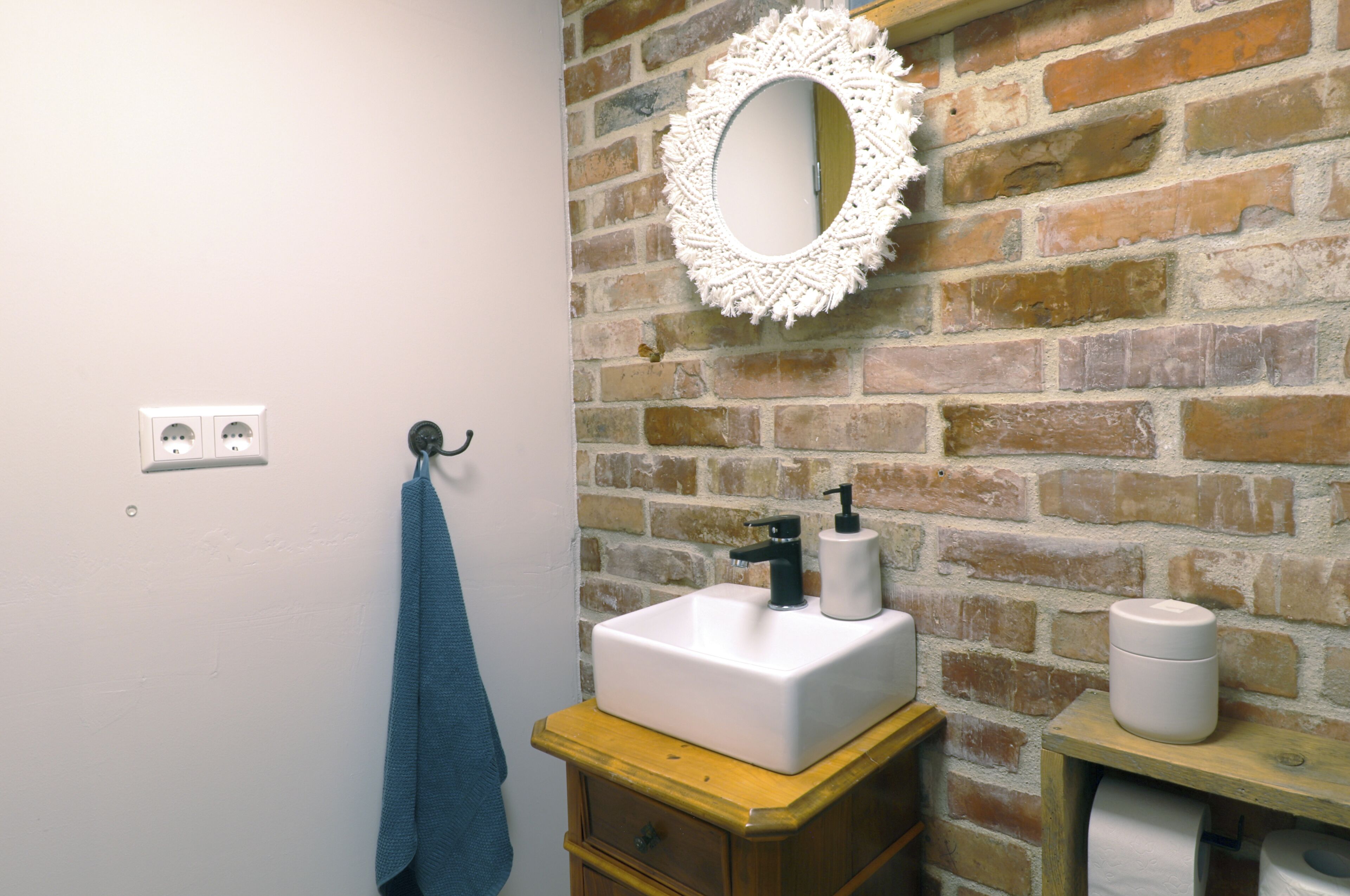 A bathroom with a white sink, a mirror, a towel, and a brick wall.