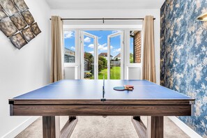 Ein Tischtennis-Tisch mit Blick durch eine offene Flügeltür in einen Garten.