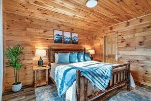 A wooden cabin bedroom with a bed, bedside lamps, a potted plant, and a door. - Hot Tub Hideaway! 5 Min to Parkway | Cozy n Quiet! (Pigeon Forge)