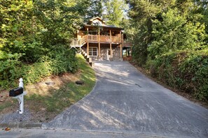 Une cabane en rondins à deux étages, dotée d’un porche et d’une allée menant à l’entrée.