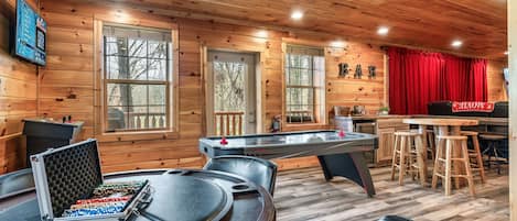 Interior de una cabaña de madera con mesa de billar, mesa de futbolín y zona de bar.