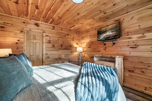 A wooden cabin room with a bed, a nightstand, a lamp, and a painting on the wall. - Hot Tub Hideaway! 5 Min to Parkway | Cozy n Quiet! (Pigeon Forge)