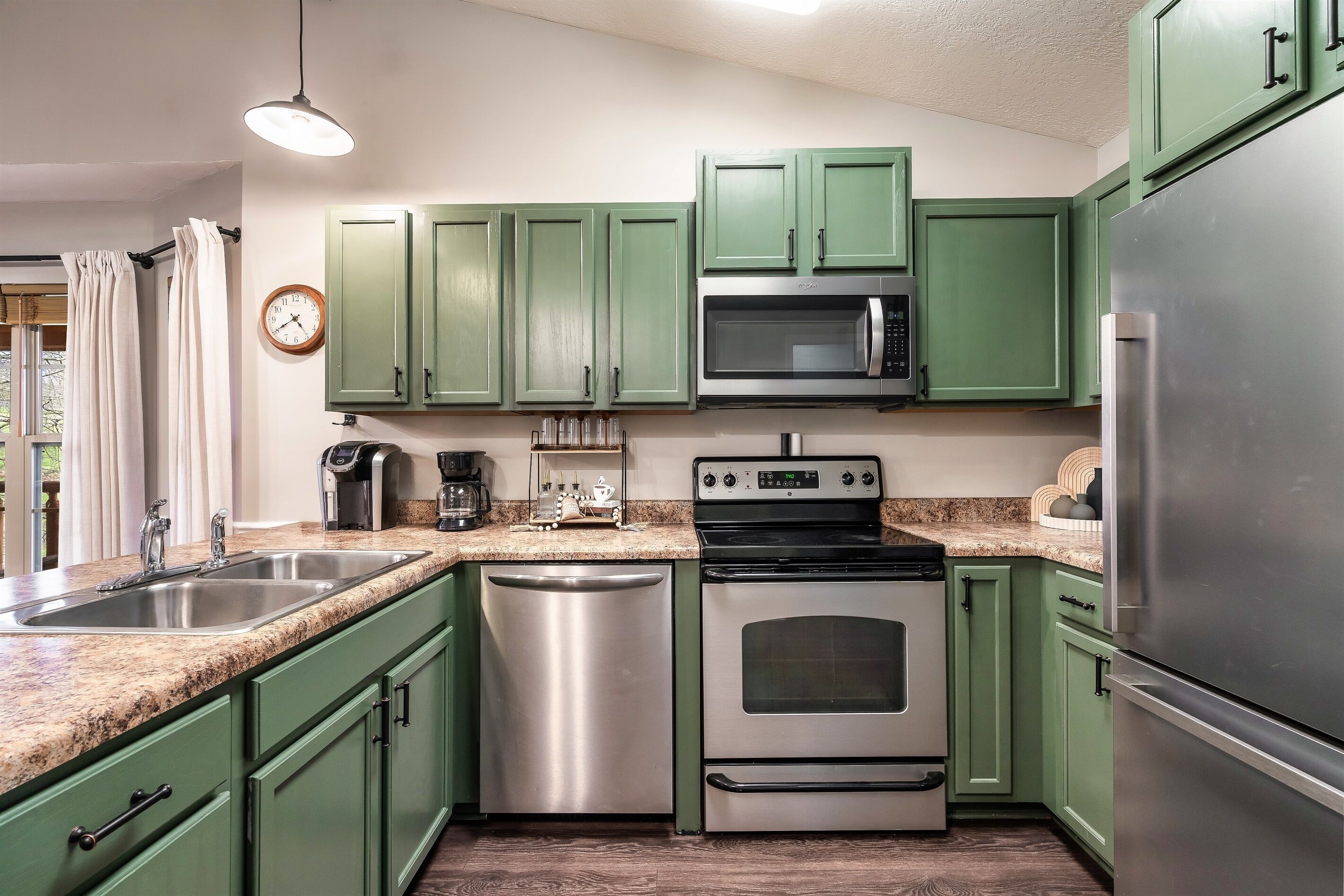 A kitchen with green cabinets, stainless steel appliances, a microwave, a coffee maker, and a dishwasher.