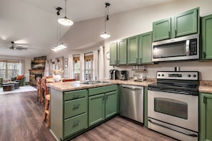 A kitchen with green cabinets, stainless steel appliances, and a dining area with a fireplace. - Hot Tub Hideaway! 5 Min to Parkway | Cozy n Quiet! (Pigeon Forge)