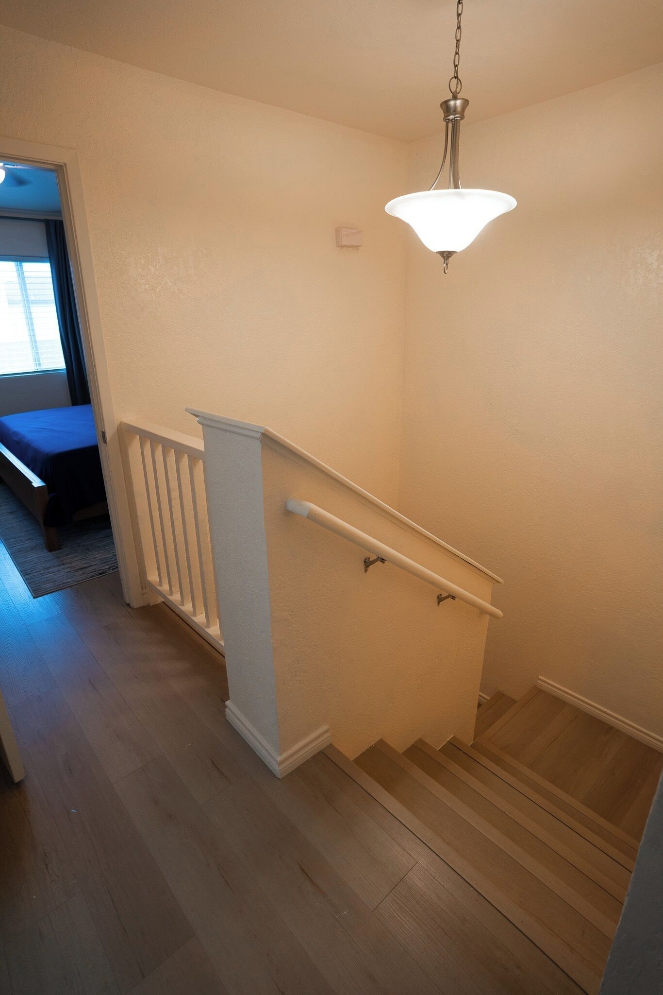 Eine Treppe mit weißer Handlauf, einer Lampe darüber und einer Tür zu einem weiteren Raum.