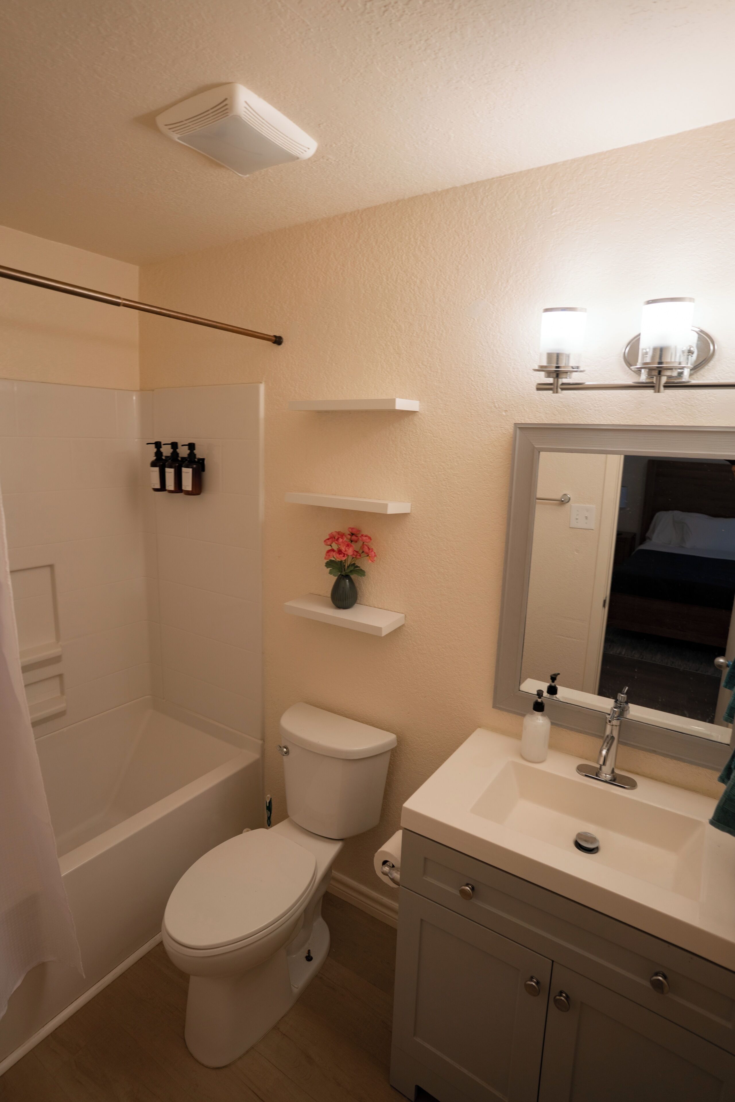 A bathroom with a bathtub, toilet, sink, and mirror. There are shelves above the sink and a shower curtain.