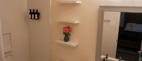 A bathroom with a bathtub, toilet, sink, and mirror. There are shelves above the sink and a shower curtain.